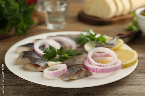 Sliced salted herring fillet served with onion rings, parsley and lemon on wooden table, closeup