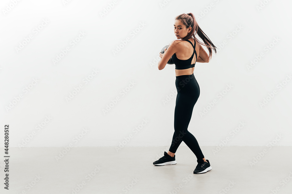 Young muscular woman doing exercises with a medicine ball against a white wall