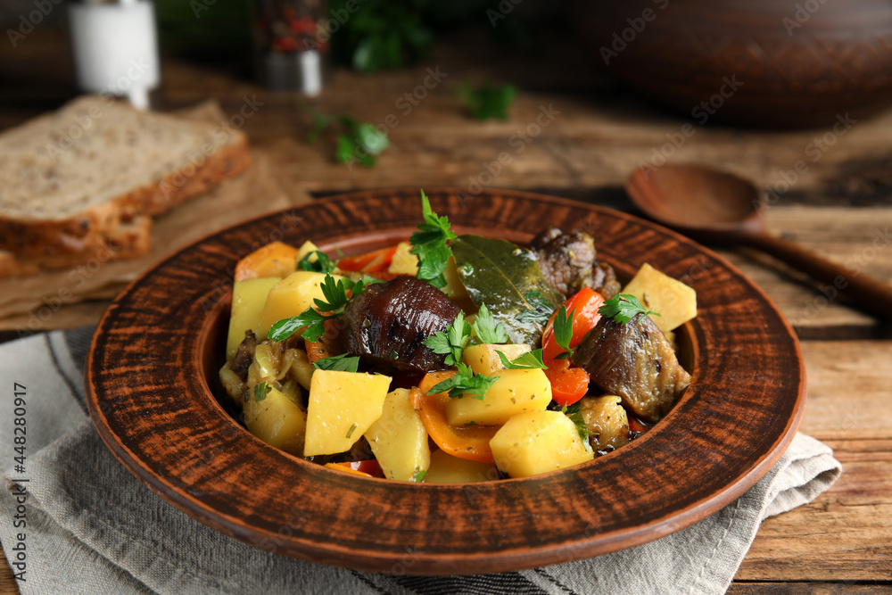 Tasty cooked dish with potatoes in earthenware served on wooden table