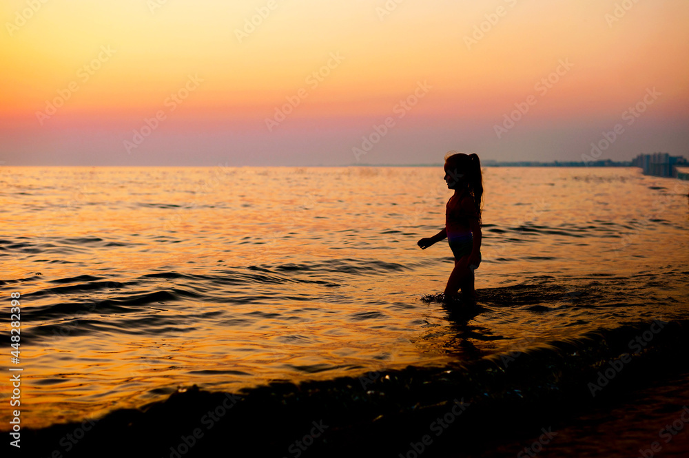 silhouette of a little girl in a swimsuit at sunset standing in the sea