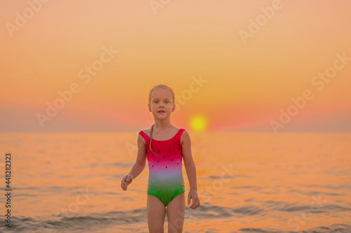 portrait of a little girl in a swimsuit with a watermelon ornament in the summer at sunset by the sea