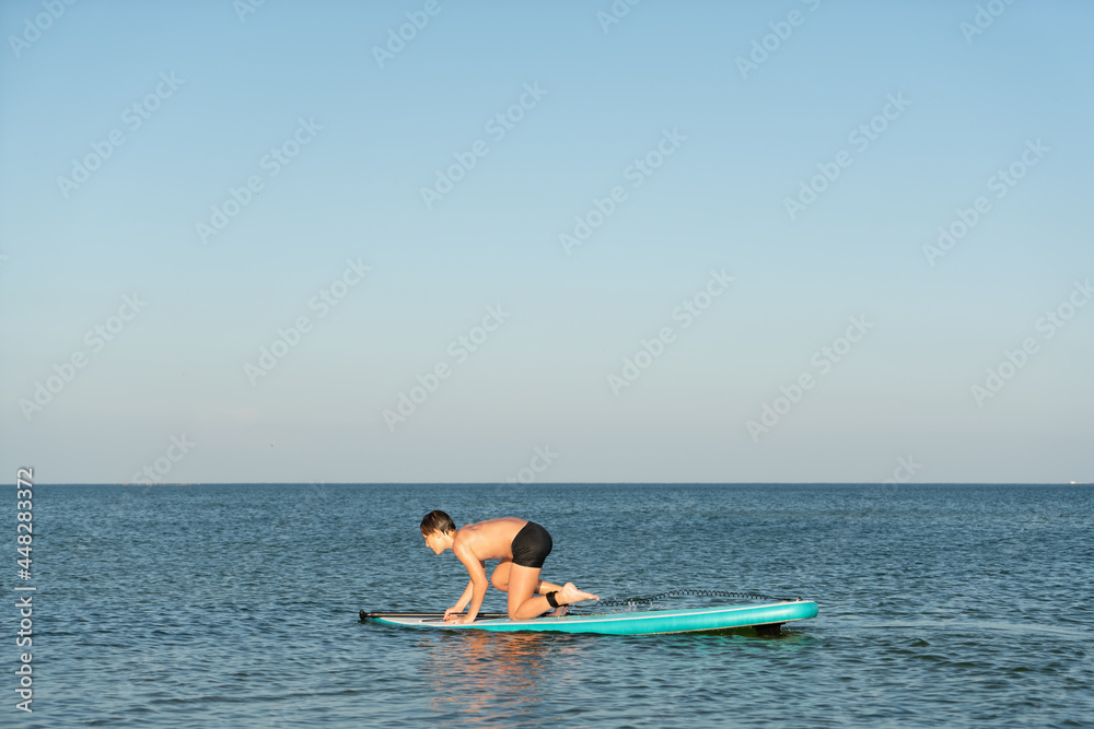 A 12 year old boy learns to stand on a SUP board in the sea near the shore.