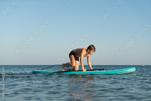 A 12 year old boy learns to stand on a SUP board in the sea near the shore.