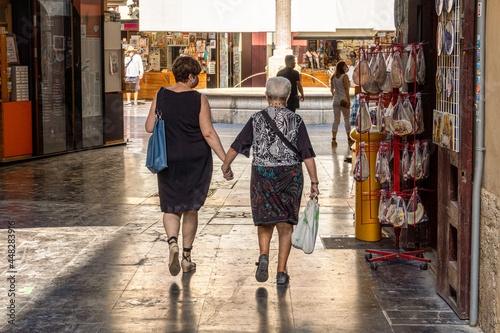 Two women holding hands walking down a pedestrian street in the city.