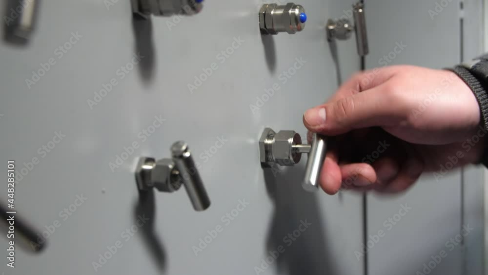 Employee hand turns shiny metal lever on control panel of machine tool in brightly lit plant workshop extreme close view