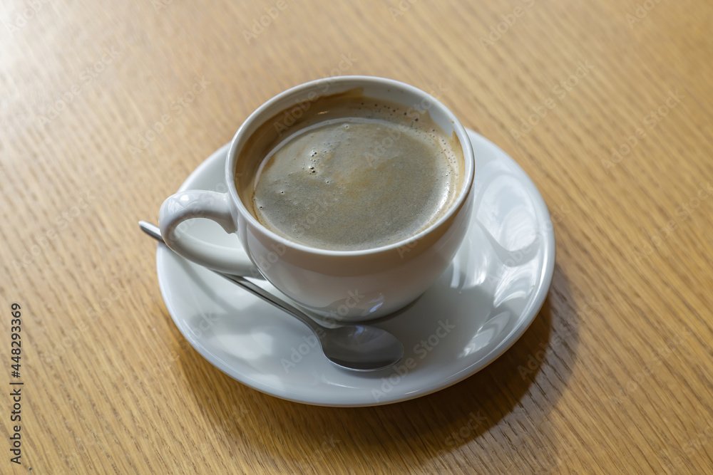 White porcelain coffee cup with saucer and spoon on wooden table in cafe White porcelain coffee cup with saucer and spoon on wooden table in cafe