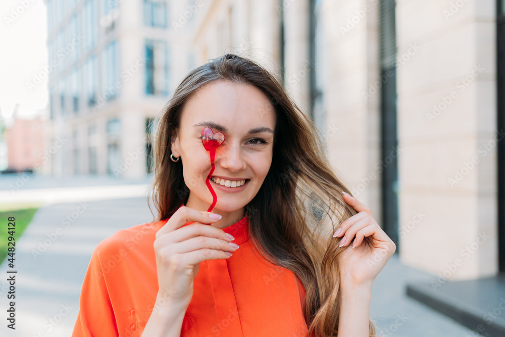 Caucasian girl smiling flirts with a heart-shaped accessory walking around the city