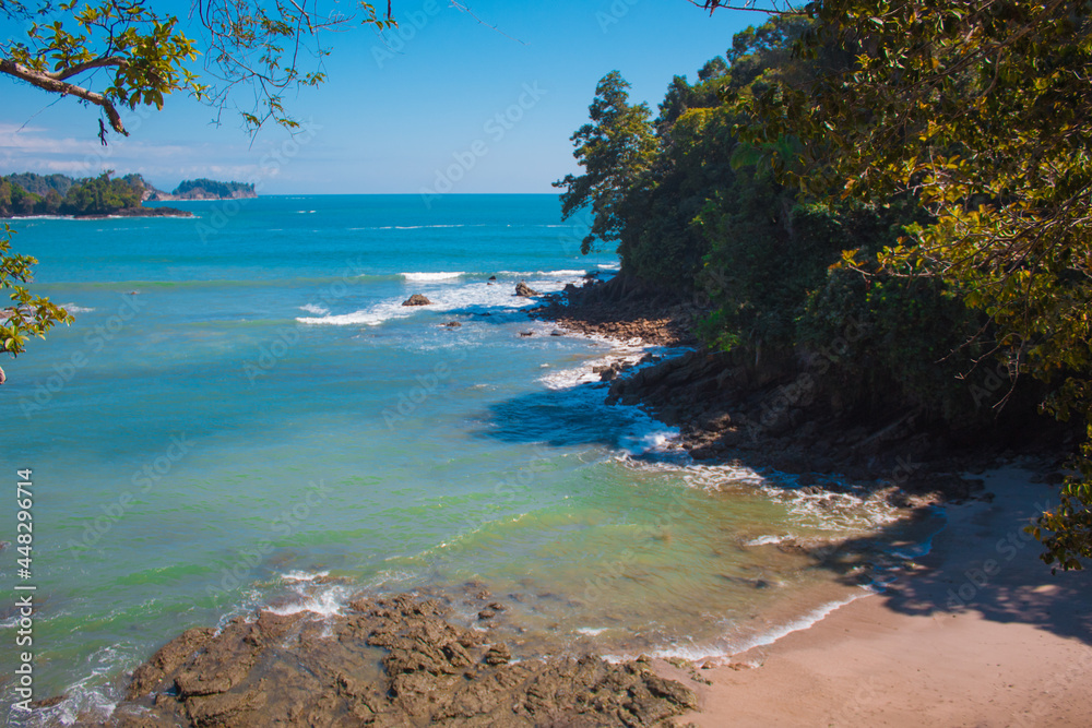 Vertical shot of a beautiful beach in the tropical pacific with white sand and blue sky surrounded by green nature in the National Park Manuel Antonio in Costa Rica