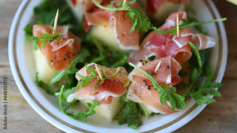 Melon jamon appetizer on a plate. Melon prosciutto salad on skewers.