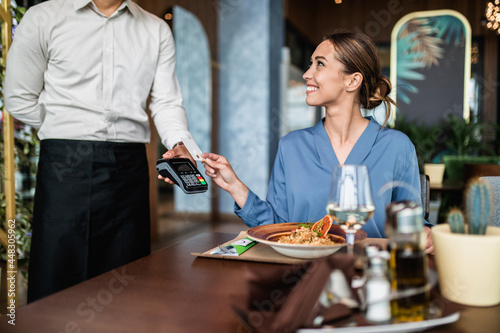 Fototapeta Beautiful young woman paying for her order with a credit card in a restaurant