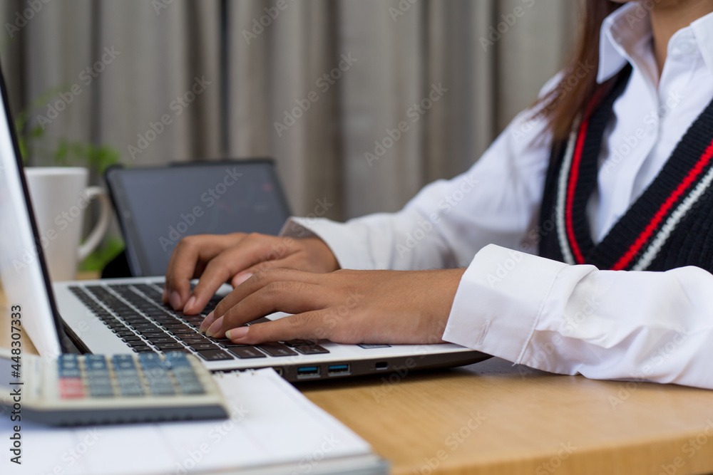 Young woman sitting, using laptop, tablet, notebook and calculator working from home. Closeup shot of unrecognizable woman, hands working on computer keyboard. Young woman sitting, using laptop, tablet, notebook and calculator working from home. Closeup shot of unrecognizable woman, hands working on computer keyboard.