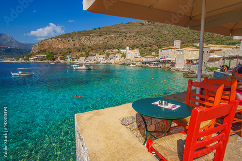 Scenic view with tables and wooden chairs by the sea at the picturesque seaside village Limeni. Traditional houses and colorful stoned buildings in Limeni, Mani area, Laconia, Greece
