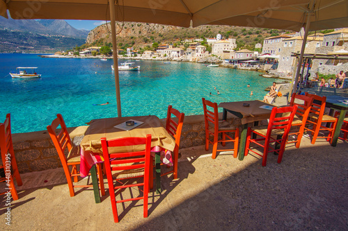 Scenic view with tables and wooden chairs by the sea at the picturesque seaside village Limeni. Traditional houses and colorful stoned buildings in Limeni  Mani area  Laconia  Greece
