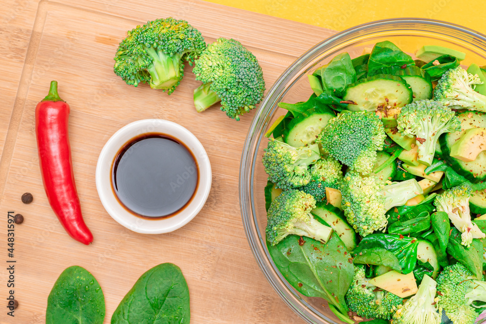 Fresh Green Salad of Avocado, Broccoli, Spinach and Cucumber with Soy Sauce and Red Hot Pepper on Wooden Cutting Board. Vegan Salad. Vegetarian Culture. Raw Food. Healthy Eating and Vegetable Diet Fresh Green Salad of Avocado, Broccoli, Spinach and Cucumber with Soy Sauce and Red Hot Pepper on Wooden Cutting Board. Vegan Salad. Vegetarian Culture. Raw Food. Healthy Eating and Vegetable Diet