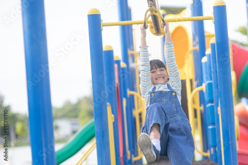 A little girl in casual clothes playing on kids playground, holding and climbing. Selective focus on girl's head.