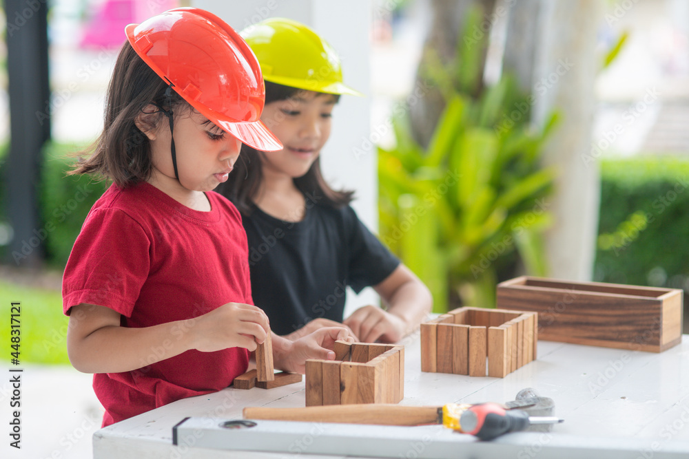 Asian Siblings girls wearing engineering hats building House from the wooden toy. To learning and enhance development, little architect.