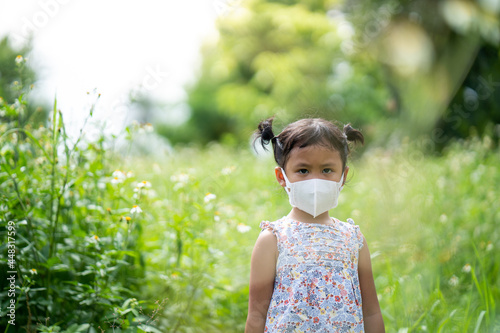 Cute small girl with protective face mask standing at field.