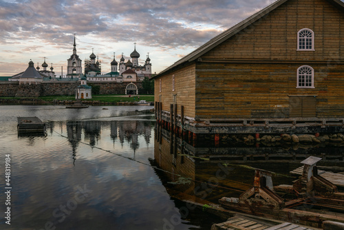 View of the rigging barn on the shore of the White Sea Bay and the Spaso-Preobrazhensky Solovetsky Monastery in the background against the sunset sky with clouds, Solovetsky Island, Arkhangelsk region