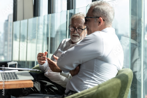 Picture of young business man discussing with his older business partner. They are in white shirt and black tie. They are sitting on a table in a hotel lobby © Attayoot