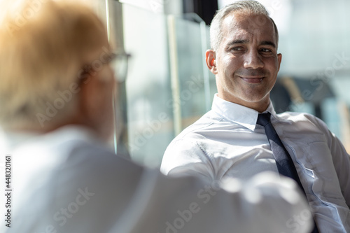 Picture of young business man discussing with his older business partner. They are in white shirt and black tie. They are sitting on a table in a hotel lobby