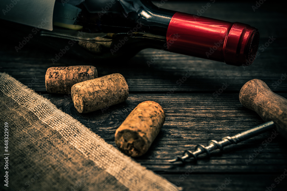 Bottle of red wine and piece of canvas with corkscrew and corks lying on an old wooden table. Close up view, focus on the bottle of red wine