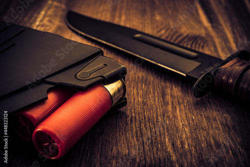 Magazine with red cartridges 12 gauge and combat knife on the wooden table. Close up view