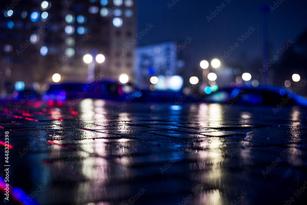 Rainy night in the big city, light from the the windows of the house is reflected in the asphalt. View from the sidewalk level paved with bricks