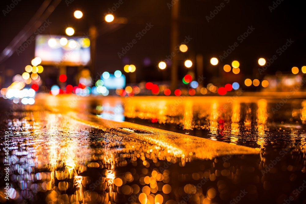 Rainy night in the big city, the light from the headlamps of vehicles approaching on the highway. View from the level of the dividing line