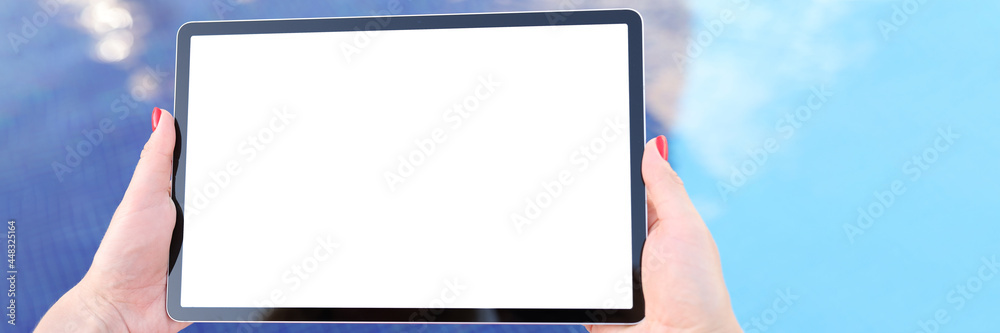 Female hands hold tablet with blank white screen above pool water Female hands hold tablet with blank white screen above pool water