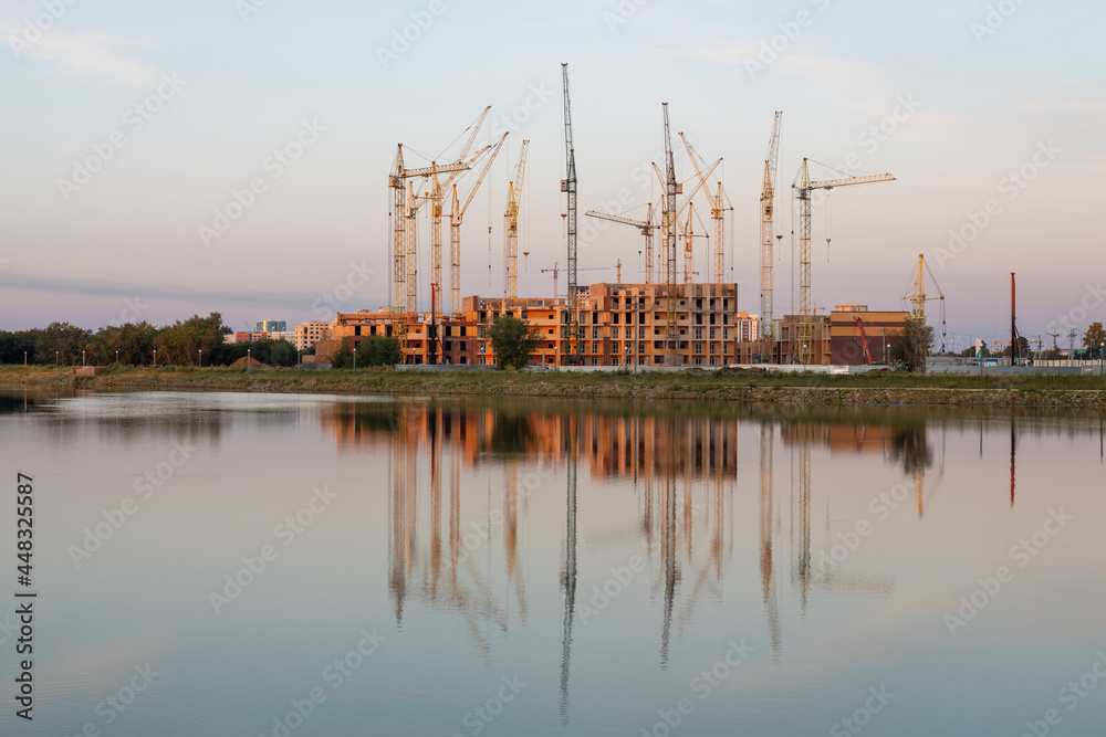 Construction site with cranes and buildings with their reflection in the water.