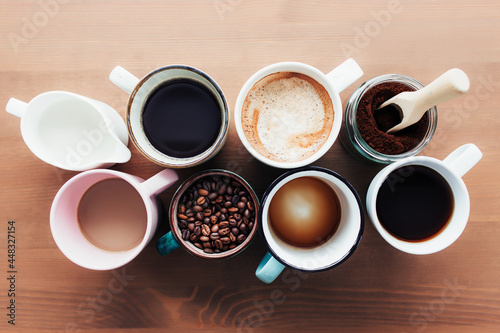 Multiple coffee cups, milk, beans and ground coffee in jar on wooden background