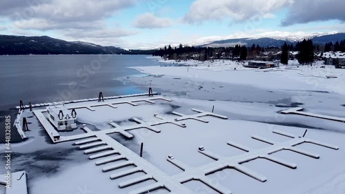 Snowy American small town in winter with frozen lake, snow covered, icy boat wharf jetty and surrounding mountains in McCall, Idaho - Aerial drone rising photo