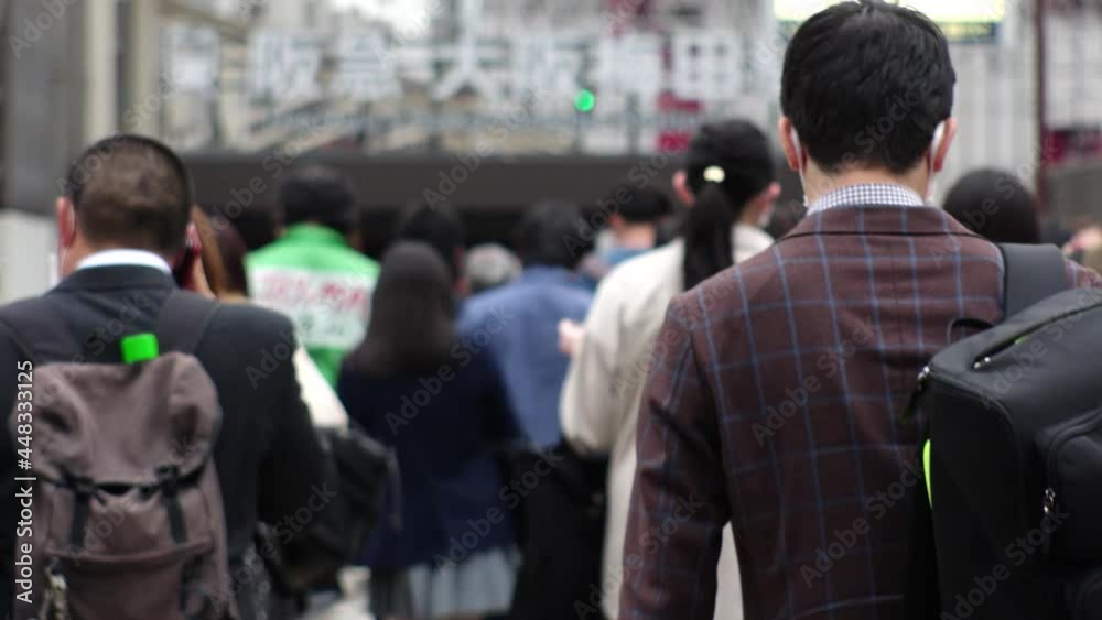 OSAKA, JAPAN - APR 2021 : Back shot of crowd of people walking down the street. View of many commuters after work near the station. Slow motion shot. Japanese city lifestyle concept. OSAKA, JAPAN - APR 2021 : Back shot of crowd of people walking down the street. View of many commuters after work near the station. Slow motion shot. Japanese city lifestyle concept.