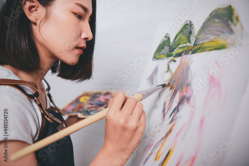 Asian woman artist painting picture with blank canvas side view, using paint brush and colour pallets having fun creativity activity occupation hobby concept, creative thinking imagination visual photo