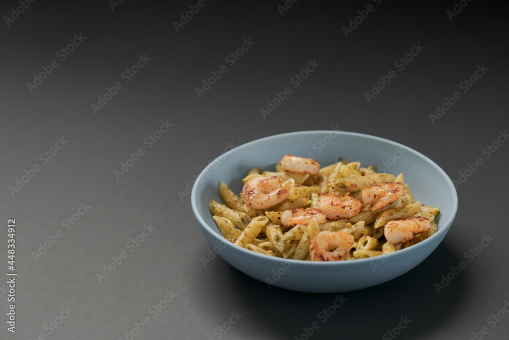 Penne pasta with shrimps and pesto in blue bowl with copy space Penne pasta with shrimps and pesto in blue bowl with copy space