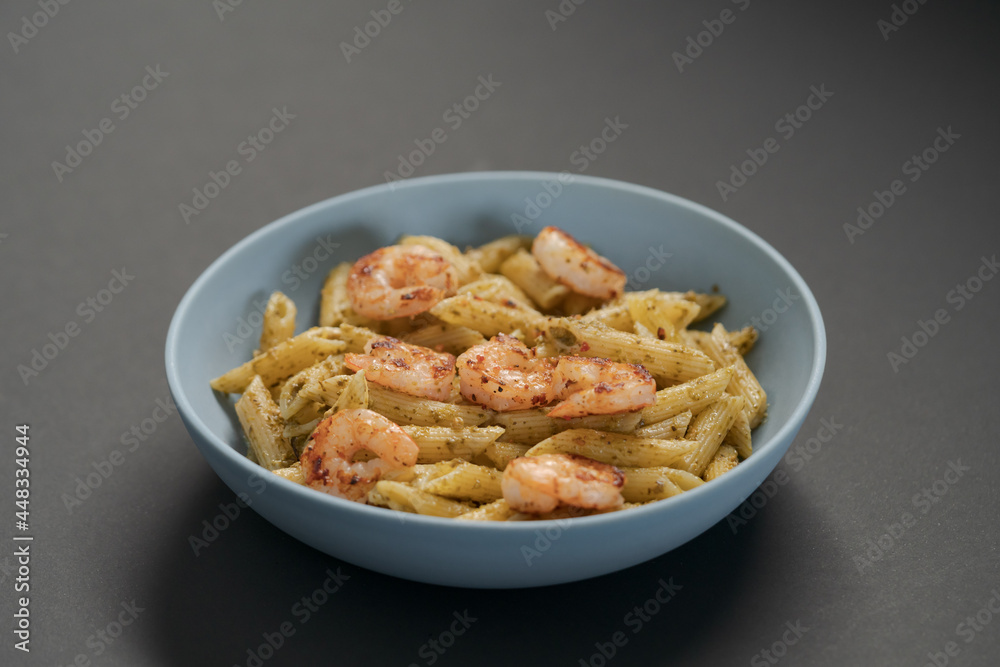Penne pasta with shrimps and pesto in blue bowl with copy space