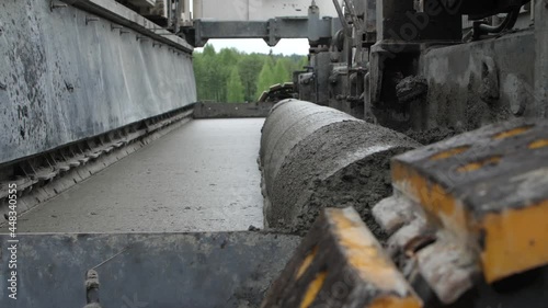 Side close-up view of road paving machine or slipform paver finisher spreading layer of concrete over roadway surface or making screed against forest in background. Concept of roadwork operation.