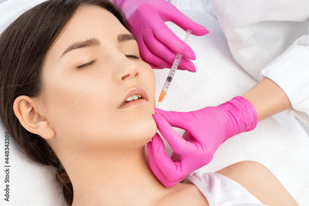 Naklejka premium Cosmetologist does injections for lips augmentation and anti wrinkle in the nasolabial folds of a beautiful woman. Women's cosmetology in the beauty salon.