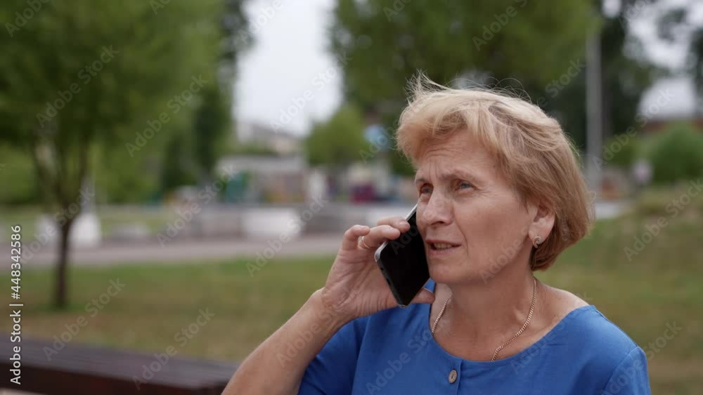 Close-up of an elderly woman talking on a mobile phone on the street in the city. An elderly female pensioner is talking on a cell phone in the open air. A phone call. Close-up of an elderly woman talking on a mobile phone on the street in the city. An elderly female pensioner is talking on a cell phone in the open air. A phone call.