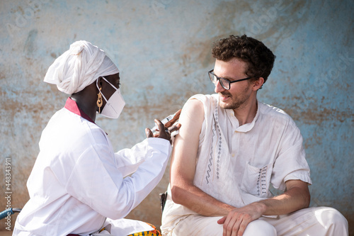 Content white caucasian healthcare worker being injected a vaccine by a black female doctor during infectious disease prevention in Africa © Riccardo Niels Mayer