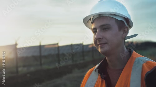 Wallpaper Mural Portrait of a young engineer next to a plantation of solar and photovoltaic panels during sunset. Checks the health and efficiency of renewable energy sources. Worker in a white helmet and vest. Torontodigital.ca