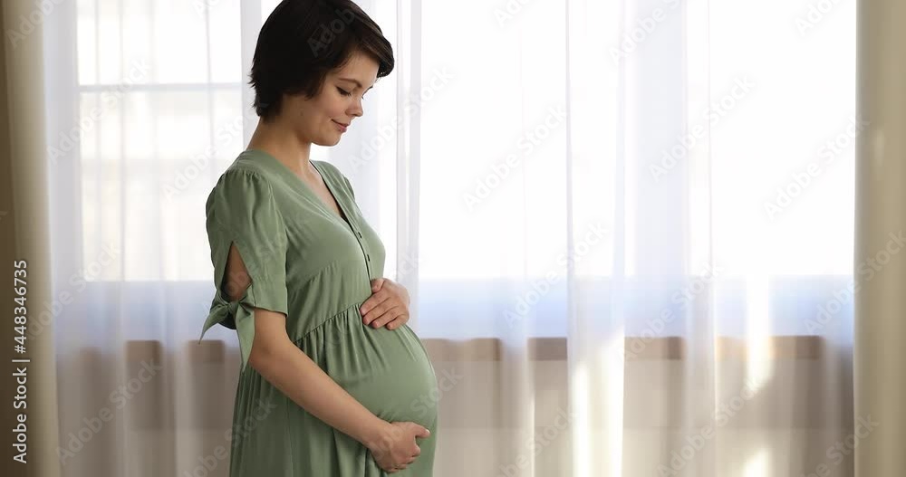 Dreamy affectionate happy millennial beautiful pregnant woman holding hands on big belly, imagining future meeting with baby, successful IVF procedure, third trimester pregnancy period concept. Dreamy affectionate happy millennial beautiful pregnant woman holding hands on big belly, imagining future meeting with baby, successful IVF procedure, third trimester pregnancy period concept.
