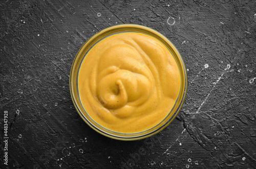 Mustard sauce in a bowl on a black stone background. Top view. Free copy space.