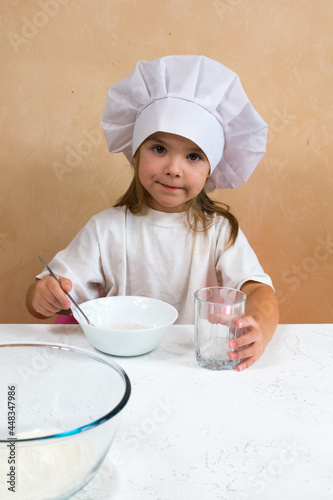 A little girl dressed as a cook kneads the dough. Child development concept. The development of fine motor skills of the hands. The kid loves, has fun, studies and plays in the kitchen