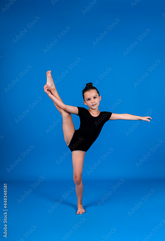 a small gymnast in a black swimsuit does stretching exercises on a blue background with a place for text