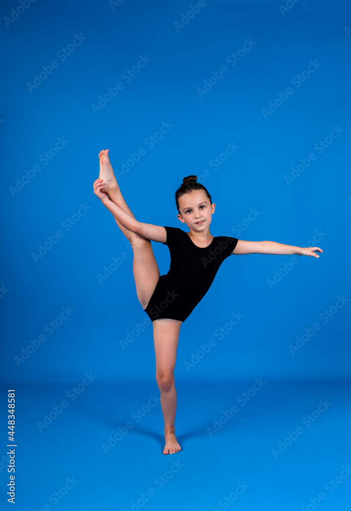 a small gymnast in a black swimsuit does stretching exercises on a blue background with a place for text a small gymnast in a black swimsuit does stretching exercises on a blue background with a place for text
