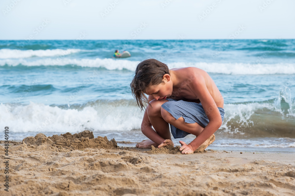 Boy on the beach plays with sand. Mediterranean sea beach, Sitges in Spain