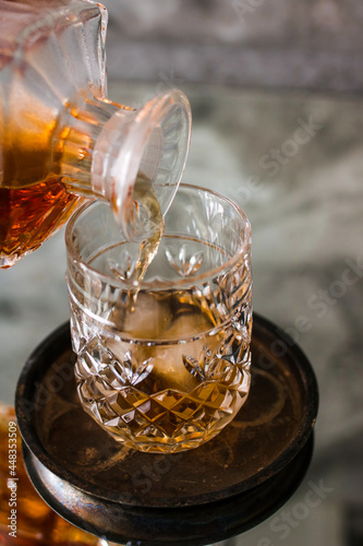 Close up pouring whiskey into drinking glass with ice cubes.