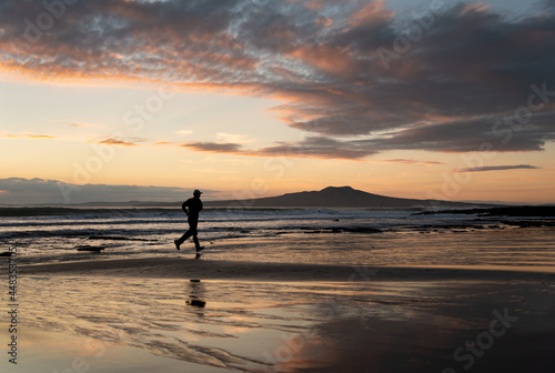 Silhouette man running on the beach at sunrise with Rangitoto Island in the background, Auckland.