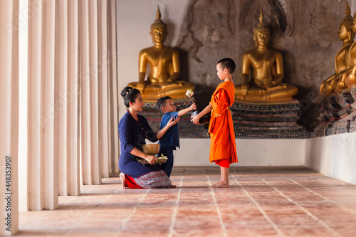 Mother and child family Thai Buddhists are giving alms to novices making merit with monk in Wat Phutthai Sawan Temple